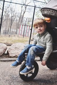 Cute boy sitting in baby stroller at park