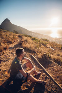 Boy sitting on landscape against sky