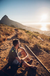 Man sitting on mountain against sky during sunset