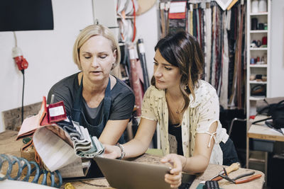 Female upholstery workers discussing over fabric swatch in workshop