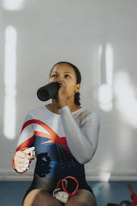 Teenage girl drinking water while sitting against wall