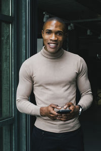 Portrait of smiling businessman with smart phone at doorway of office