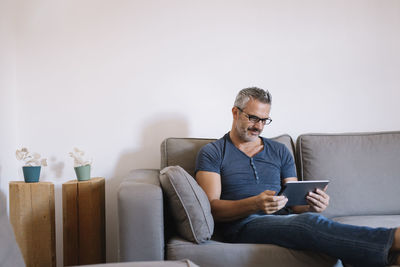 Mature man sitting on couch at home using tablet
