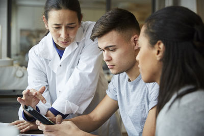 Mature teacher with young students using calculator in engineering classroom