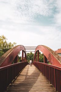 Back of woman cycling on footbridge against sky