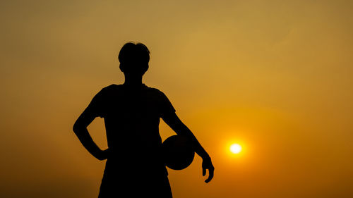 Silhouette man standing against orange sunset sky