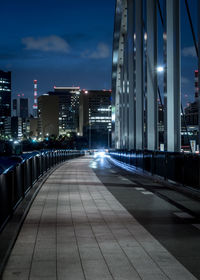 Illuminated street amidst buildings against sky at night