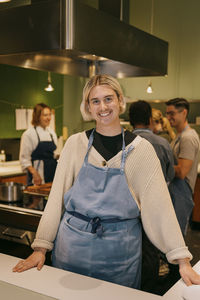 Portrait of smiling non-binary student wearing apron while standing in kitchen during cooking class