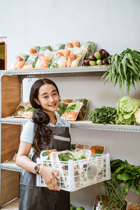 Portrait of smiling young woman standing by vegetables on table