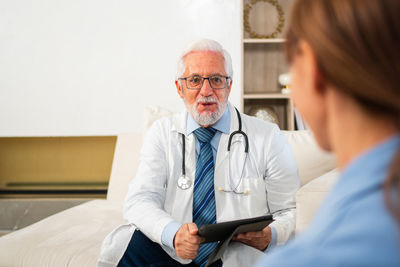 Portrait of doctor holding stethoscope while sitting on bed at home