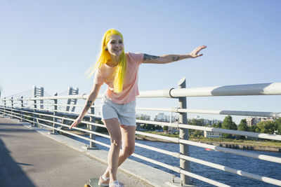 Full length portrait of woman standing by railing against sky