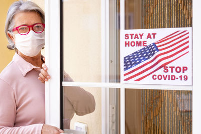 Portrait of woman wearing mask standing at house entrance