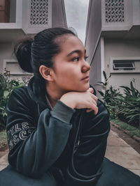 Portrait of young woman looking away while sitting on building