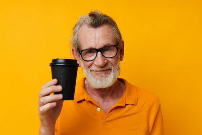 Portrait of young woman holding drink against yellow background