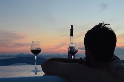 Close-up of woman holding beer glass against sea during sunset