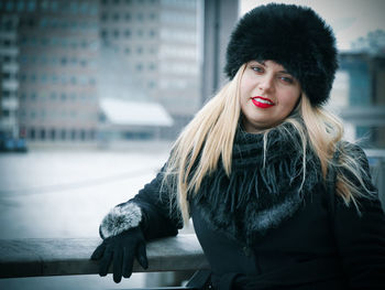 Portrait of young woman in fur hat standing against buildings