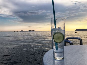 Glass of water on table by sea against sky