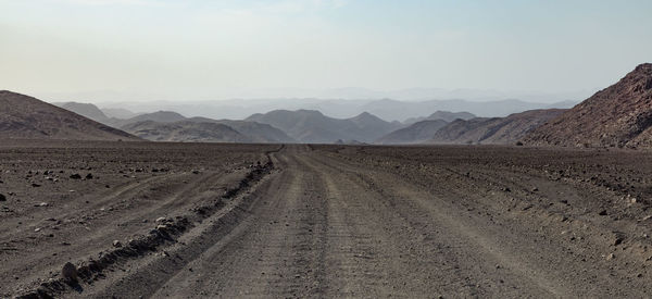 Dirt road amidst desert against sky
