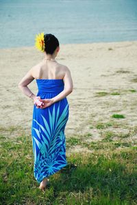 Rear view of woman wearing blue dress and flower walking at beach