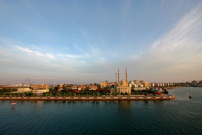 City at waterfront against sky during sunset