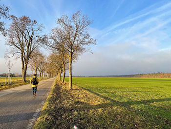 Man on road amidst field against sky