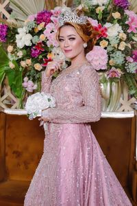 Portrait of beautiful young woman standing by pink flowering plants