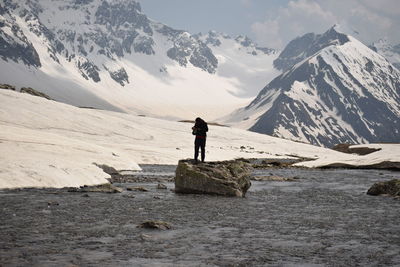 Man standing on rock against snowcapped mountains