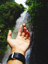 Cropped image of hand against waterfall