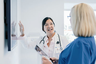 Female doctor gesturing at flat screen while discussing with colleague in hospital