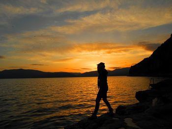 Silhouette woman walking at beach against sky during sunset