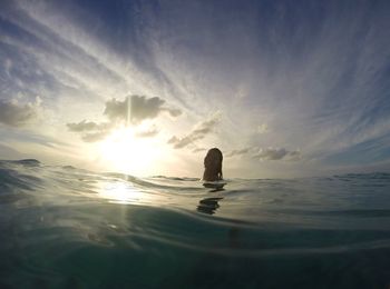 Woman swimming in sea against sunset sky