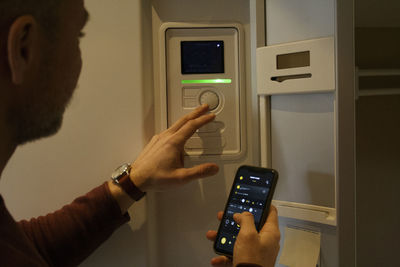 Man adjusting temperature through thermostat while holding smart phone