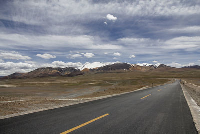 A flat and uninhabited asphalt road leads to the distant snowy mountains