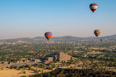 Hot air balloons flying over landscape against clear sky