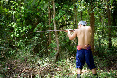 Rear view of shirtless man standing in forest