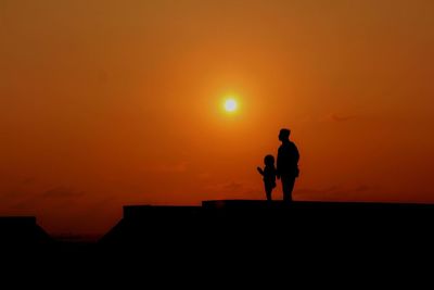 Silhouette father and son standing against orange sky