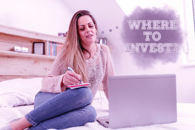 Young woman using mobile phone while sitting on laptop