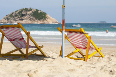 Deck chairs on beach against sky