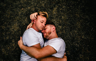 High angle view of gay couple embracing while lying on grass outdoors