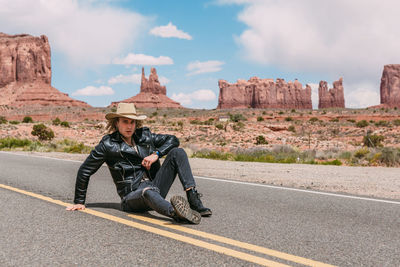 Man sitting on road against sky