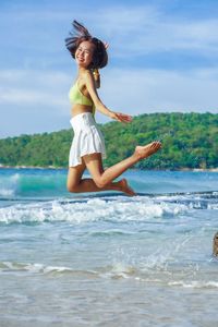 Rear view of young woman jumping in sea against sky