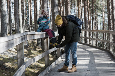 Father helping his daughter put on her shoe whilst walking in the wood