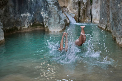 Anonymous crop travelers diving into clean lake and splashing water while having fun during vacation in summer