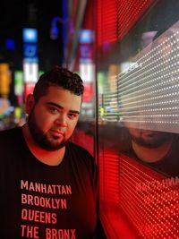Portrait of bearded man standing by store window in illuminated city