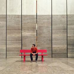 Man sitting on bench against wall