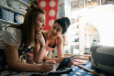 Female owners discussing while using digital tablet by window in fabric shop