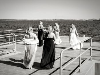 Rear view of female friends walking on pier over sea against clear sky