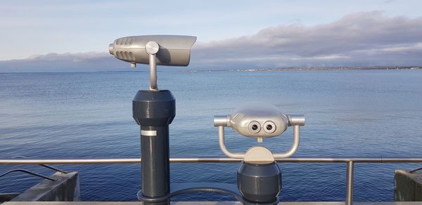 Coin-operated binoculars by sea against sky