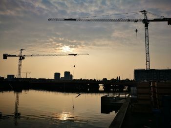 Silhouette cranes at construction site against sky during sunset