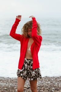 Woman wearing red jacket standing at beach